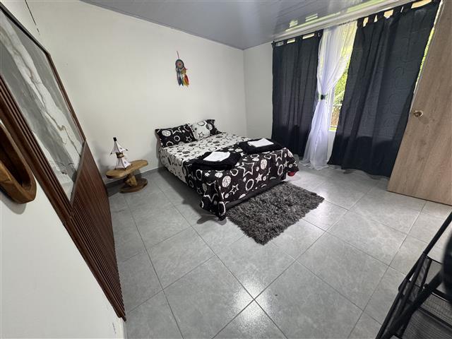 ecohotelgaia11 Alquiler Fincas Quindio Hoteles Eje Cafetero Planes Transporte Small bedroom with a double bed in blackandwhite bedding a grey rug wooden nightstand with a lamp a dreamcatcher on the wall and a large window with black and sheer curtains