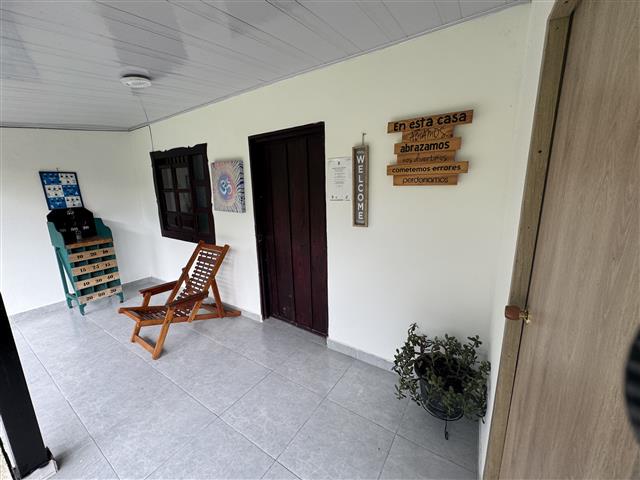 ecohotelgaia21 Alquiler Fincas Quindio Hoteles Eje Cafetero Planes Transporte Covered porch with a wooden lounge chair potted plant a colorful cabinet and wall signs including a'WELCOME' banner and a Spanish message.