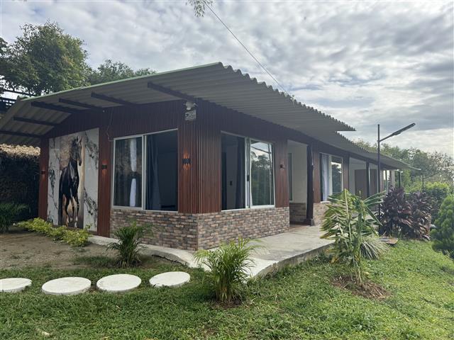 ecohotelgaia3 Alquiler Fincas Quindio Hoteles Eje Cafetero Planes Transporte Exterior view of a single story building with corrugated metal roof brick base and large glass doorswindows surrounded by green plants and a grassy yard